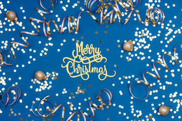 Wall Mural - Holiday background with Merry Christmas wording, golden confetti, balls and ribbons on classic blue. Holiday celebration card concept