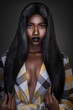 © Phil - A portrait of a serene young black female with long black hair, beautiful makeup, popping dark lip stick posing by herself wearing a colorful coat in front of a dark background.