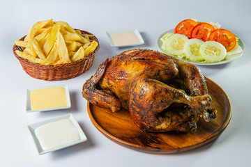 Delicious whole grilled chicken with french fries, salad and creams on wooden plate. Peruvian food 