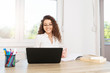 © Bojan Topalovic - Happy brunette in white shirt sitting in office by the window, wearing glasses and looking at laptop.