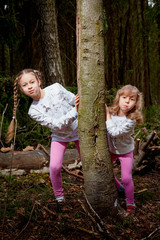 Two young girl playing and having fun together on walk in forest outdoors. Happy loving family with two sisters or female friends posing on nature landscape with with pine trees.