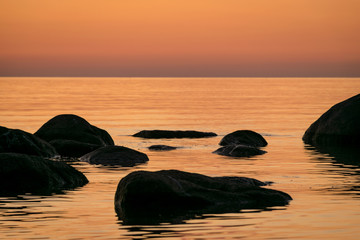 orange sunset by the sea, black stone silhouettes against the sea background, summer