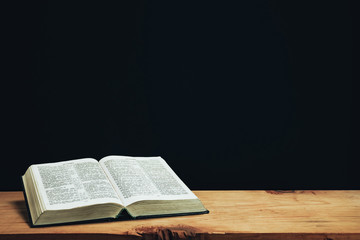 Aufkleber - Open Holy Bible on a red old wooden table. Beautiful Black wall background..