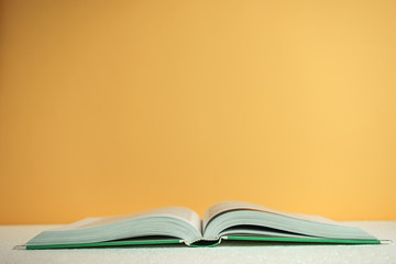 Poster - Beautiful open book on a white table and orange wall background behind.