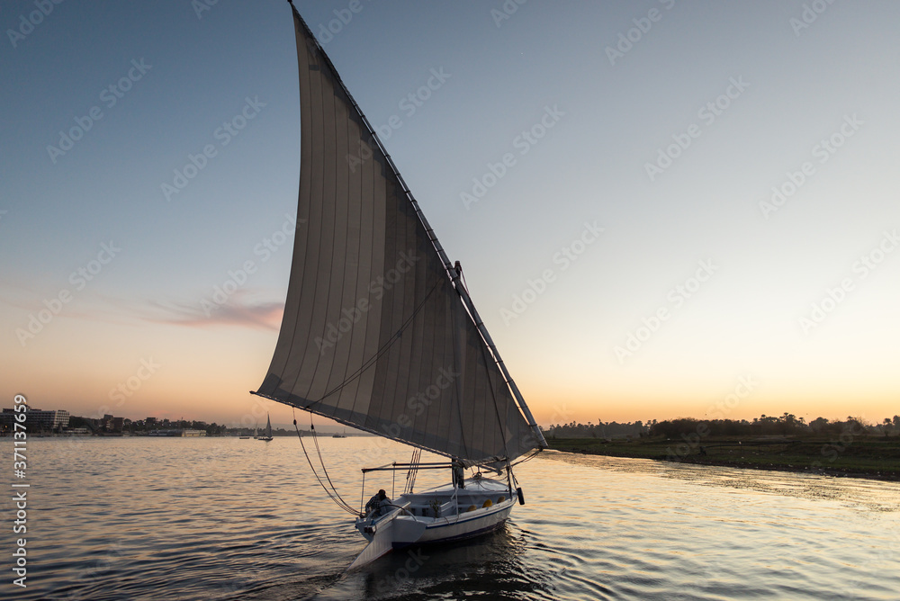 A felucca traditional wooden sailing boat used in Egypt sailing in Nile river during sunset - obrazy, fototapety, plakaty 