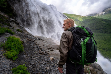 man hiking with backpack looking at waterfall. portrait of male adult back standing outdoor.