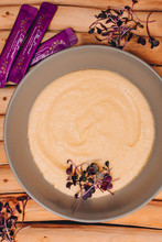 Keto Plain Porridge On A Wooden Background, With Some Purple Leaves Next To The Bowl And In The Porridge With Some Premium Black Current Powder