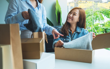 Wall Mural - Two young women receiving and opening a postal parcel box of clothing at home for delivery and online shopping concept