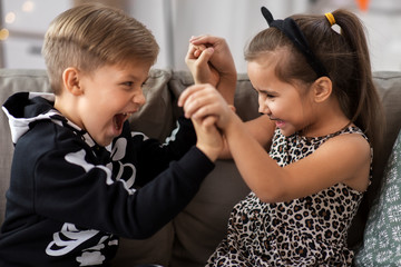 Poster - halloween, holiday and childhood concept - smiling little boy and girl in costumes having fun at home