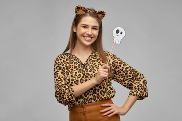 Wall Mural - holiday, photo booth and people concept - happy smiling woman in halloween costume of leopard with ears and scull party accessory over grey background