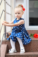 Wall Mural - little girl sits in a blue dress on the steps. pin up style