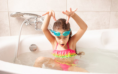 Funny little girl in a swimsuit and swimming goggles depicts a sea monster bathing at home in the bathroom. Concept of entertainment for children and the desire to go on a summer vacation