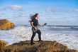 © serejkakovalev - Young male in black and long hair play on guitar on the beach