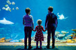 © Irina Schmidt - Two kids boys and toddler girl visiting together zoo aquarium. Three children watching fishes and jellyfishes. School boys wearing medicals masks due pandemic corona virus time. Family on staycation