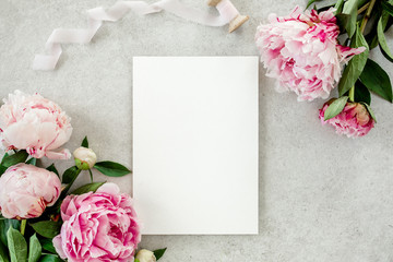 Mockup invitation, blank paper greeting card and peonies on gray stone table. Flower background. Flat lay, top view.