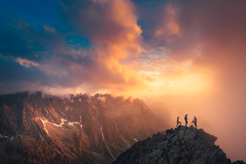 Team success concept photo, friends standing together on the top of the hill, over beautiful mountains landscape in gold sunset light, orange edit space..