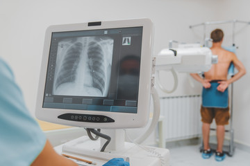 Young caucasian man standing against wall while doctor using X-Ray machine scan him in hospital