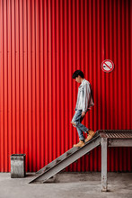 Young Asian Man Walking Down From Stairs Against Red Background