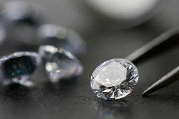 brilliant cut diamond held by tweezers on black background