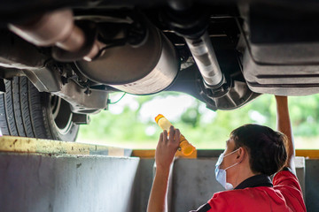 Mechanic with lamp is checking the bottom of SUV car in garage automobile service.