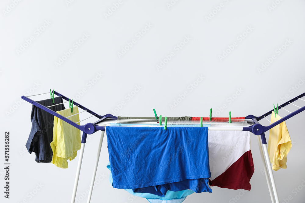 Clean clothes hanging on dryer against light background
