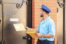 Handsome Young Postman Putting Letters In Mail Box Outdoors