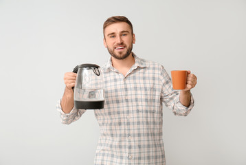 Wall Mural - Young man with electric kettle and cup on light background