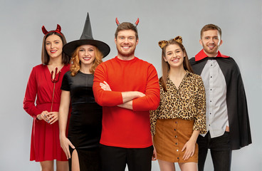 Wall Mural - friendship, holiday and people concept - group of happy smiling friends in halloween costumes of vampire, devil, witch and leopard over grey background