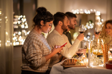 Wall Mural - holidays and people concept - woman with smartphone at dinner party with friends at home