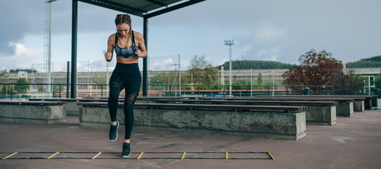 Young sportswoman training jumping on an agility ladder outdoors