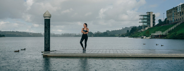 Sticker - Young sportswoman looking at the lake from the pier under the rain