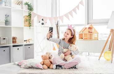 Cute little girl taking selfie with teddy bear in light room