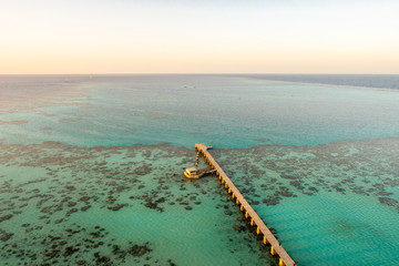 Sanganeb Reef National Park in Sudan, Red Sea, aerial view from Sanganeb Lighthouse with old wooden pier extending towards the sea, azure crystal water and endless horizon.