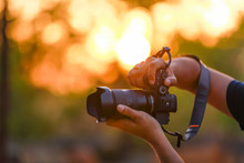 Closeup Of A Black Camera Holding By Photographer's Hand With Sunset Background
