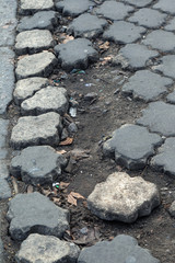 Sticker - Damaged road with potholes, caused by freeze-thaw cycles in winter. Bad road. Broken pavements paving slabs on sidewalk. Pavement with paving slabs with defects and cracks coming in perspective.