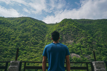 young indian boy standing in the edge of the balcony, enjoying the scenic view of the green mountains.