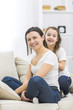 © Andrii - Happy smiling mother and daughter sitting on sofa.