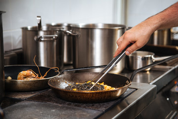 Wall Mural - Chef cooking black pasta in a pan with tongs