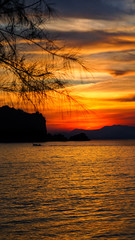 Wall Mural - A beautiful setting sun behind the hills and rocks with its reflection over the sea waves at Tanjung Rhu Beach, Langkawi,