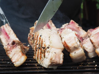 a cook in a black apron roasts steaks meat on the bone. grilled pork on the bone. tongs for grilling.