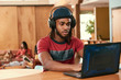© SuperStock - Portrait of young ethnic man wearing red t shirt and knit hat wearing headphones, sitting at bar in kitchen of downtown loft with laptop computer
