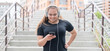 A fat young woman goes down the stairs and listens to music on a smartphone. Obese girl with headphones resting after jogging.