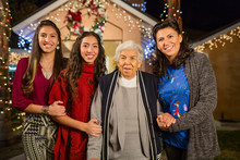 Three Generations Of Hispanic Women Smiling Outside House Decorated With String Lights