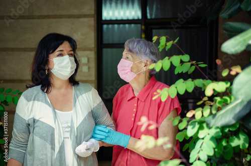 Cuadros en Lienzo Two neighbors in protective masks and rubber gloves have just left the entrance of the house