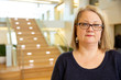 © SuperStock - Portrait of middle aged woman wearing glasses standing by stairwell in lobby of building, smiling looking towards camera