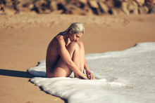 Naked Wet Young Woman Sitting At Shore During Sunny Day, Contemplating