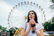 © Westend61 - Young woman drinking soft drink while standing against Ferris wheel in amusement park