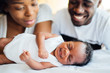 © Westend61 - Close-up of smiling parents looking at newborn daughter sleeping on bed