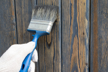 A worker painting a wooden wall. A man holding brush. A hand of worker painting wooden plank. A painter with paint brush