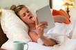 © SuperStock - Coughing young woman in her bed with using tablet to check in with doctor
